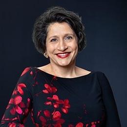 Person wearing black and red shirt standing in front of dark background smiling